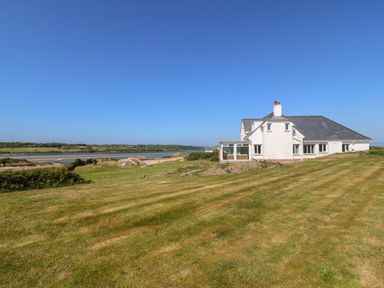 A white house with a lawn and water in the background at Wig Carna in Holyhead