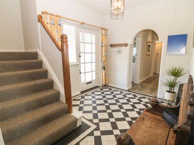 An entryway with carpeted stairs a checkerboard tiled floor a wooden bench and a potted plant at Wig Carna in Holyhead
