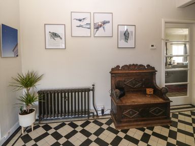 A room with a vintage wooden bench a radiator potted plant framed marine animal prints and a tiled floor at Wig Carna in Holyhead