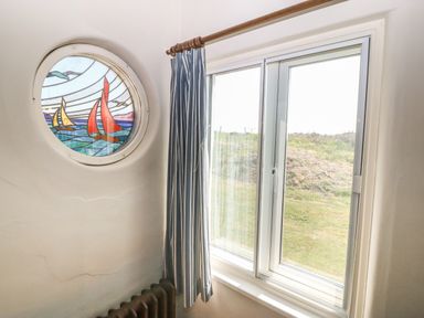 A corner of a room with a round stained glass window, a sliding glass window with curtains, and part of a radiator at Wig Carna in Holyhead