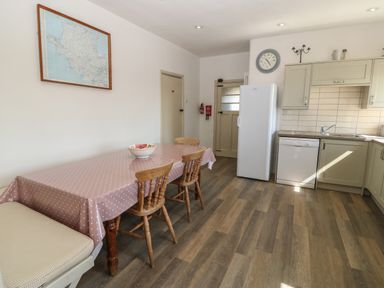A kitchen with a dining table covered with a polka dot tablecloth three wooden chairs a white refrigerator dishwasher and sink at Wig Carna in Holyhead
