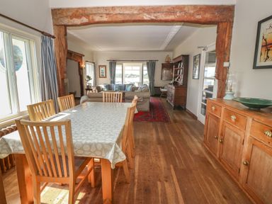 A dining area with a table and chairs next to a living room with sofas and a cabinet at Wig Carna in Holyhead