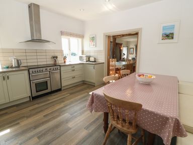 A kitchen with a dining table covered with pink polka dot tablecloth and wooden chairs next to a stove and countertop with appliances at Wig Carna in Holyhead