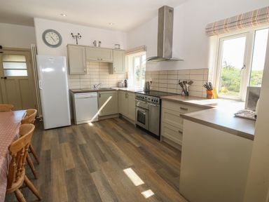 A kitchen with wooden chairs around a table and white cabinets and appliances at Wig Carna in Holyhead