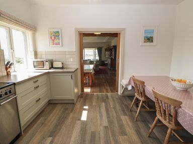A kitchen with cabinets microwave toaster table with cloth and chairs leading to a dining area at Wig Carna in Holyhead