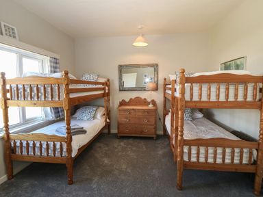 A bedroom with two wooden bunk beds a wooden dresser with a lamp and a mirror on the wall at Wig Carna in Holyhead