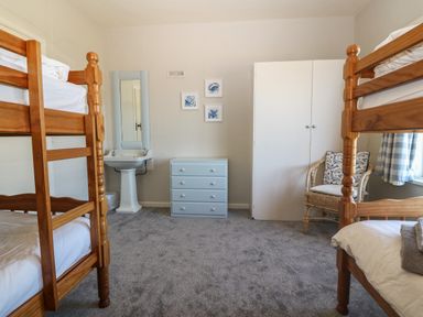 A bedroom with two wooden bunk beds a white wardrobe a blue chest of drawers a washbasin with mirror and a wicker chair at Wig Carna in Holyhead