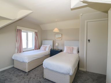 A bedroom with two single beds a window with striped curtains and a nightstand at Wig Carna in Holyhead