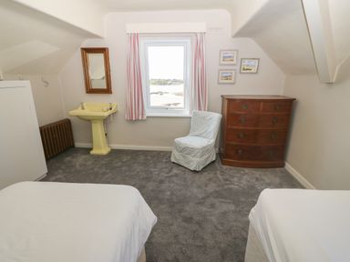 A bedroom with two beds a yellow sink a window with curtains a wooden chest of drawers and a chair at Wig Carna in Holyhead