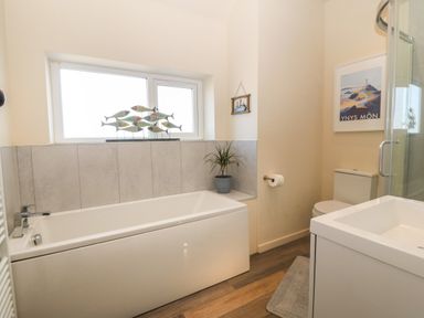 A bathroom with a bathtub under a window with fish decorations a toilet a shower a sink a plant and framed pictures at Wig Carna in Holyhead