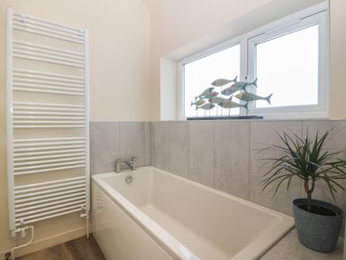 A bathroom with a bathtub a white towel radiator a window with fish decorations and a potted plant at Wig Carna in Holyhead