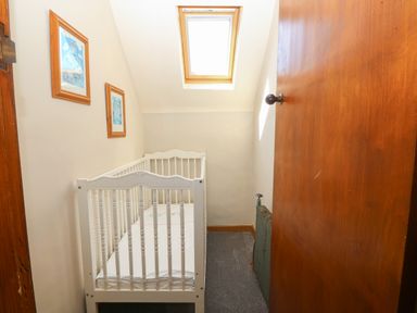 A small room with a white baby crib a skylight window and two framed pictures on the wall at Wig Carna in Holyhead