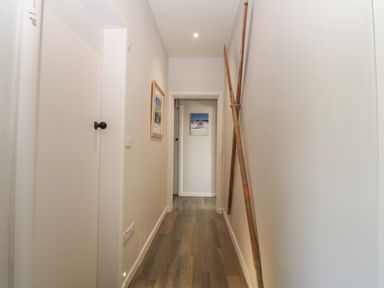 A narrow hallway with wooden floorboards picture on the left wall and two wooden oars leaning against the right wall at Wig Carna in Holyhead