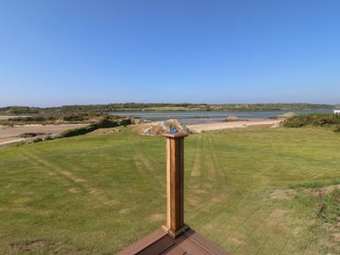 A grassy lawn with rocks and a body of water beyond under a clear blue sky at Wig Carna in Holyhead