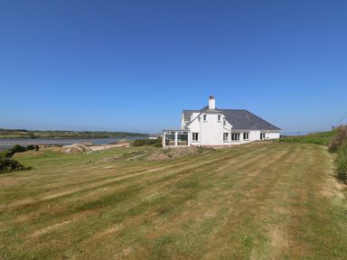 A house with a large grassy yard near a body of water at Wig Carna in Holyhead