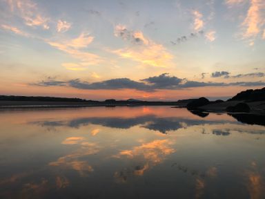 A body of water reflecting a sunset sky with clouds and a distant shoreline at Wig Carna in Holyhead