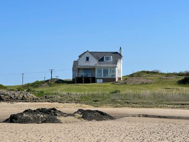 A house with a grassy lawn and rocks in the foreground at Wig Carna in Holyhead