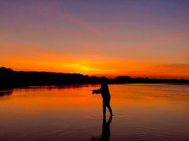 A person fishing in shallow water during sunset at Wig Carna in Holyhead