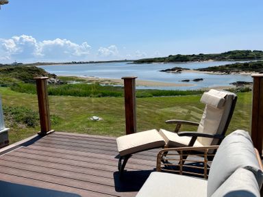 A wooden deck with cushioned chairs overlooking a grassy area and a body of water at Wig Carna in Holyhead