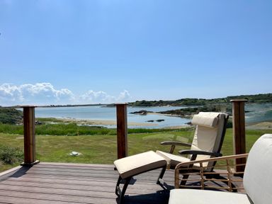 A wooden deck with cushioned chairs overlooking a grassy area and a body of water at Wig Carna in Holyhead
