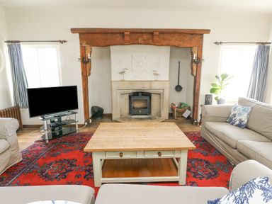 A living room with a wooden coffee table a red patterned rug beige sofas a fireplace and a television at Wig Carna in Holyhead