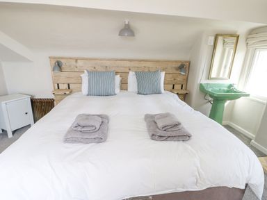 A bedroom with a wooden headboard bed two pillows gray towels a green sink and a mirror at Wig Carna in Holyhead