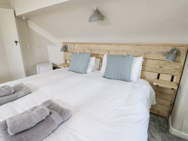 A bedroom with a large bed with wooden headboard two striped pillows and folded towels on the bed at Wig Carna in Holyhead
