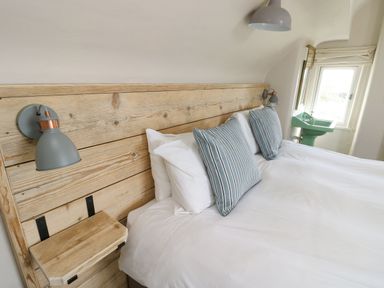A bedroom with a wooden headboard and two blue striped pillows next to a green sink under a window at Wig Carna in Holyhead