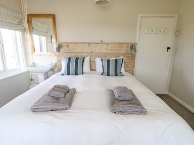 A bedroom with a double bed white bedding gray towels a wooden headboard and a sink with mirror at Wig Carna in Holyhead