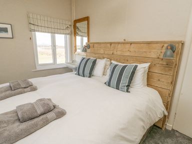 A bedroom with a wooden headboard a bed with striped pillows and towels near a window with a mirror hanging on the wall at Wig Carna in Holyhead