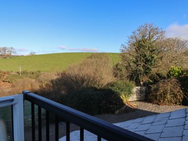A view of a green hill with sheep and trees seen from a balcony with black railing at Fern Cottage in Muddiford near West Down