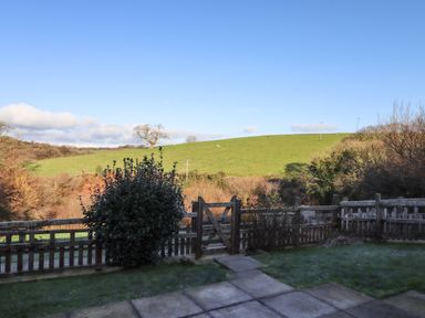 A garden with a wooden gate and fence overlooking a grassy hill at Fern Cottage in Muddiford near West Down