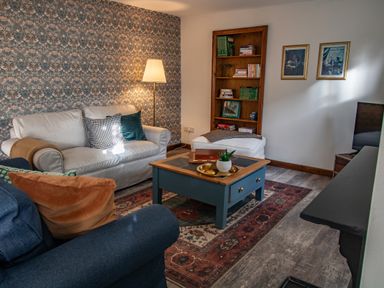 A living room with sofas a blue table a floor lamp and a bookshelf at Fern Cottage in Muddiford near West Down