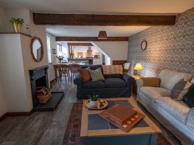 A living room with sofas a coffee table and a fireplace opening into a dining area and kitchen at Fern Cottage in Muddiford near West Down