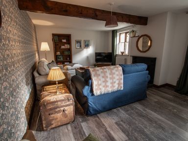 A living room with blue and beige sofas a wooden bookshelf a TV and a lamp on a vintage trunk at Fern Cottage in Muddiford near West Down