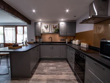 A kitchen with grey cabinets black countertops and wooden floor at Fern Cottage in Muddiford near West Down