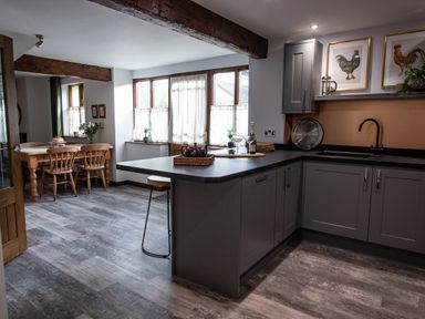 A kitchen and dining area with gray cabinets wooden dining table and chairs and framed rooster pictures at Fern Cottage in Muddiford near West Down