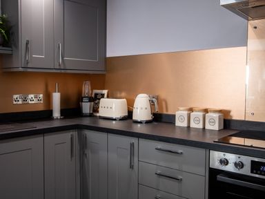 A kitchen corner with grey cabinets a toaster kettle blender paper towel holder and labeled jars at Fern Cottage in Muddiford near West Down