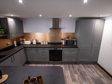 A kitchen with gray cabinets a black countertop and appliances including a microwave toaster kettle and oven at Fern Cottage in Muddiford near West Down