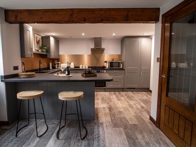 A modern kitchen with a grey island and two wooden stools at Fern Cottage in Muddiford near West Down