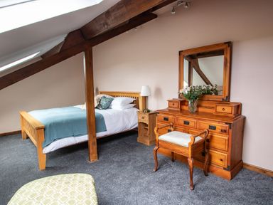 A bedroom with wooden bed side table and dresser with mirror and stool at Fern Cottage in Muddiford near West Down