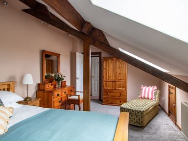 A bedroom with a bed a wooden dresser with a mirror a chair a wardrobe and a chaise lounge at Fern Cottage in Muddiford near West Down