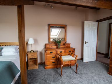 A bedroom with wooden dresser mirror chair bedside table and a bed at Fern Cottage in Muddiford near West Down
