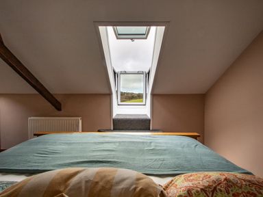 A bedroom with a bed facing a skylight window and a radiator on the wall at Fern Cottage in Muddiford near West Down