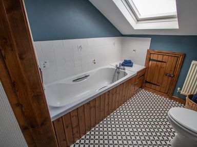 A bathroom with a bathtub wooden paneling a tiled floor a skylight window and a toilet at Fern Cottage in Muddiford near West Down