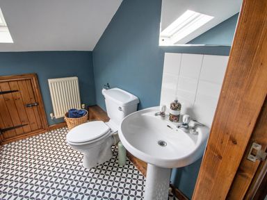 A bathroom with a toilet sink wooden door and patterned floor tiles at Fern Cottage in Muddiford near West Down