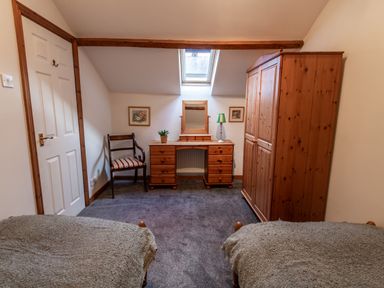 A bedroom with two beds a wooden wardrobe a dressing table a chair and a skylight window at Fern Cottage in Muddiford near West Down