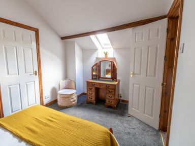 A bedroom with a wooden vanity table a round chair two white doors and a bed with a yellow blanket at Fern Cottage in Muddiford near West Down