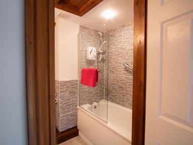 A bathroom with a bathtub shower tiled walls and a red towel at Fern Cottage in Muddiford near West Down