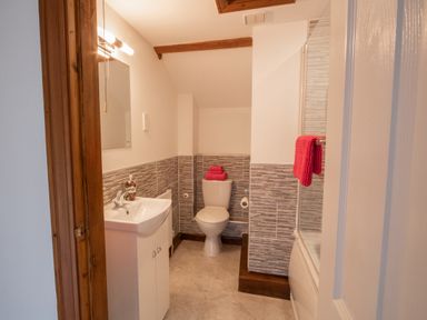 A bathroom with a sink, mirror, toilet, and bathtub with red towels at Fern Cottage in Muddiford near West Down